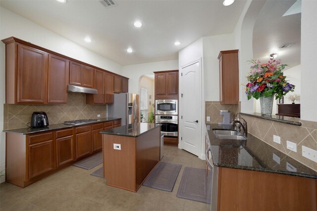 kitchen featuring decorative backsplash, arched walkways, a sink, dark stone countertops, and stainless steel appliances