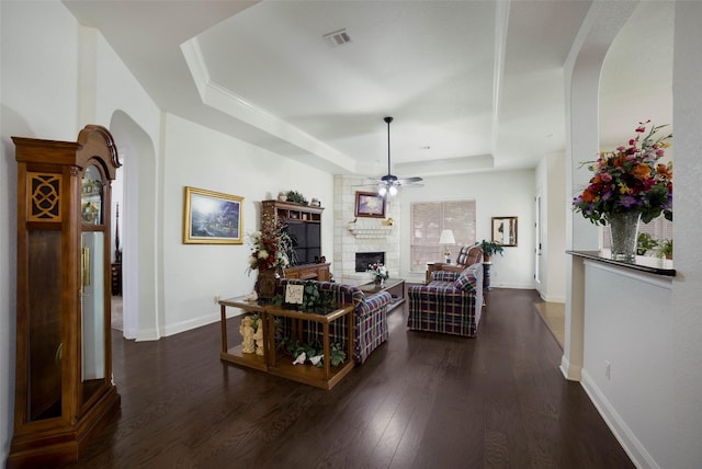 living room with ceiling fan, dark wood-style flooring, visible vents, arched walkways, and a raised ceiling