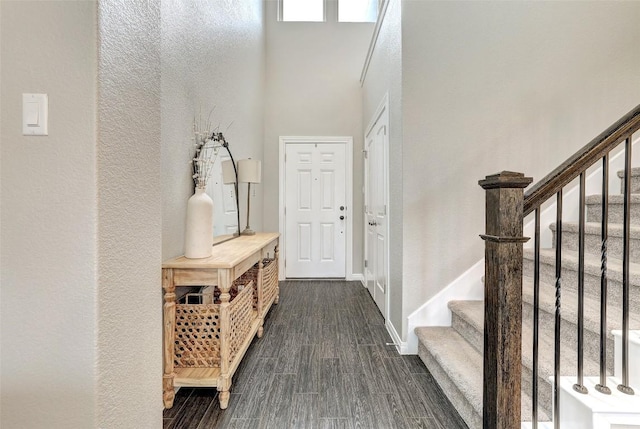 mudroom with a textured wall, dark wood-style floors, baseboards, and a towering ceiling