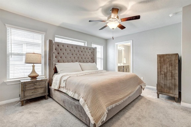 bedroom featuring a ceiling fan, baseboards, light colored carpet, and ensuite bathroom