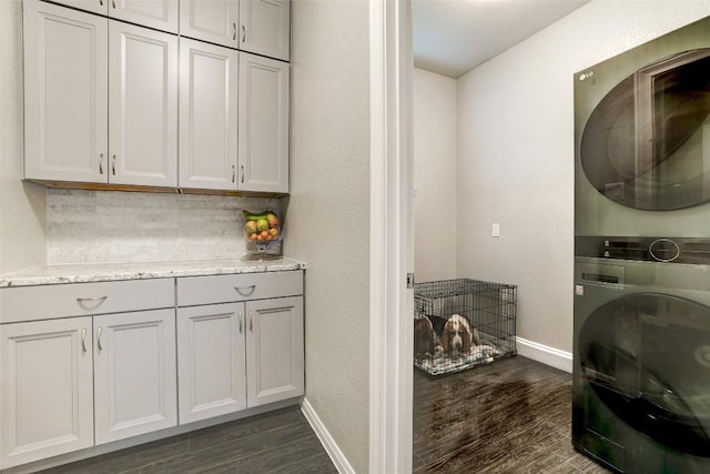 laundry area with baseboards, cabinet space, stacked washer / drying machine, and dark wood-style floors