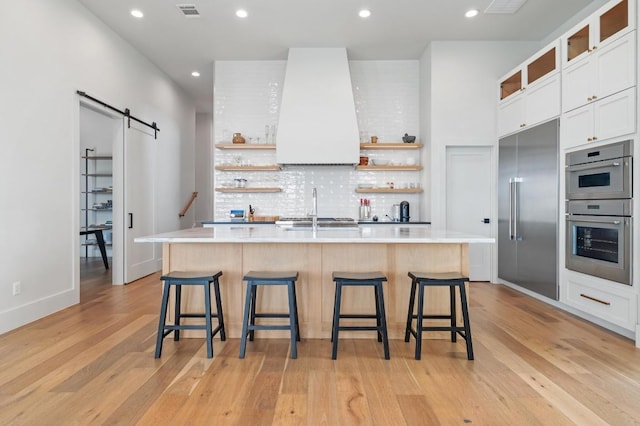 kitchen with open shelves, wall chimney exhaust hood, a barn door, and visible vents