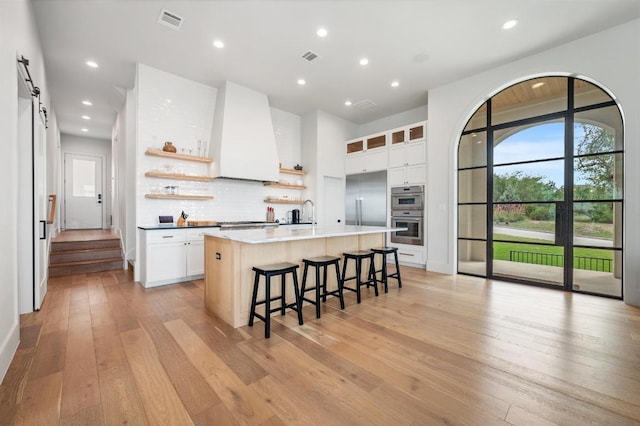 kitchen featuring visible vents, open shelves, a kitchen breakfast bar, light wood finished floors, and stainless steel appliances