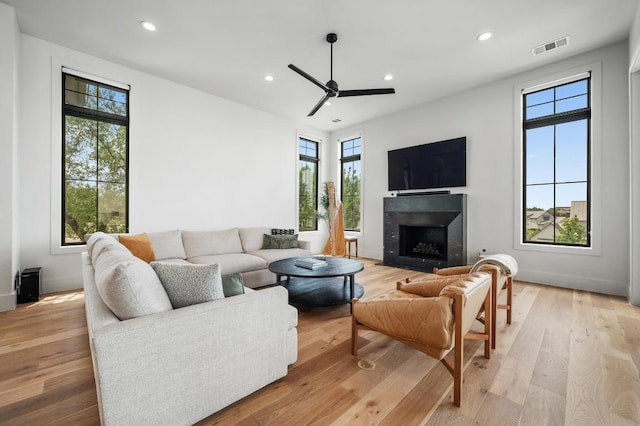 living area featuring a ceiling fan, recessed lighting, a fireplace with flush hearth, light wood-type flooring, and visible vents
