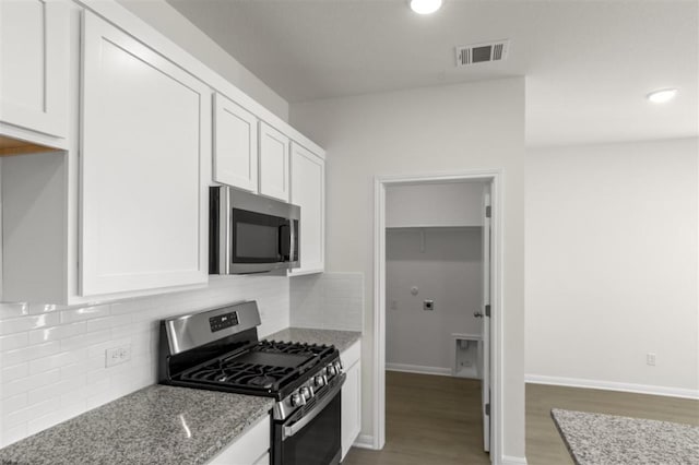 kitchen featuring white cabinets, light stone countertops, appliances with stainless steel finishes, wood finished floors, and visible vents