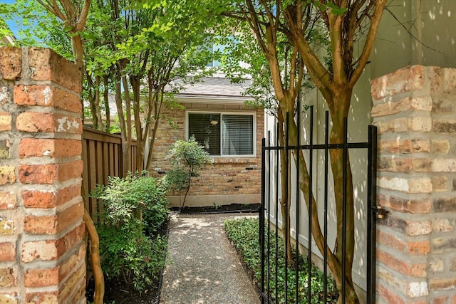 view of side of home featuring brick siding, a gate, fence, and a shingled roof