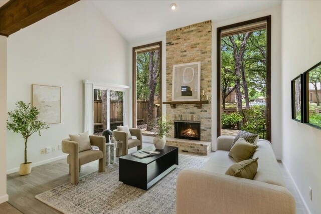 living area with a brick fireplace, baseboards, wood finished floors, and high vaulted ceiling