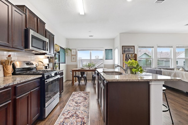 kitchen with an island with sink, a kitchen bar, tasteful backsplash, a sink, and stainless steel appliances