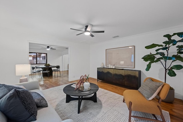living area featuring visible vents, a ceiling fan, crown molding, and wood finished floors