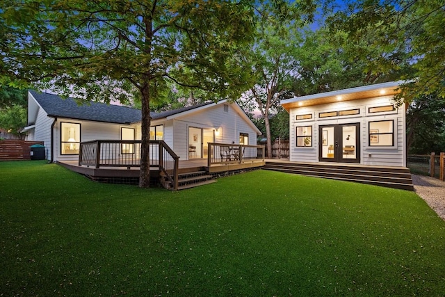 rear view of house with fence, french doors, a wooden deck, a lawn, and an outdoor structure