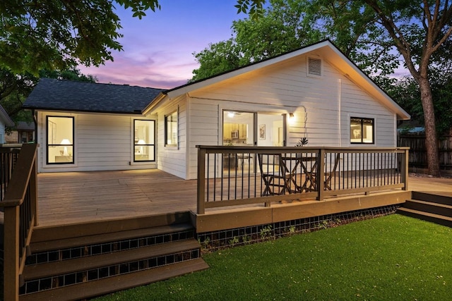 rear view of house featuring roof with shingles, a wooden deck, and a yard