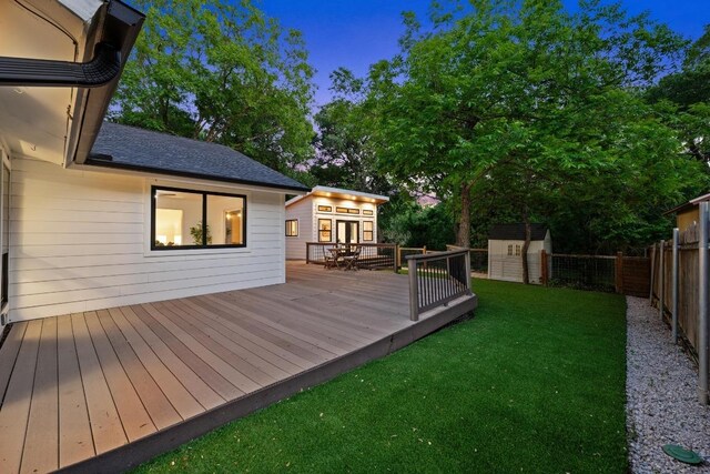 wooden deck with a lawn, a storage unit, an outbuilding, and a fenced backyard