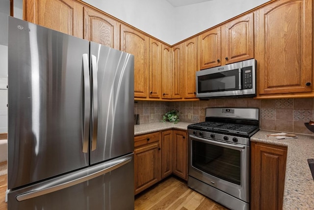 kitchen featuring stainless steel appliances, brown cabinetry, light wood-style flooring, and tasteful backsplash