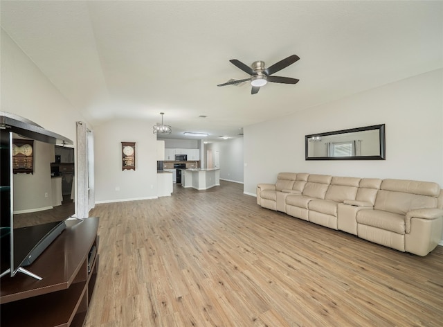 living area featuring baseboards, vaulted ceiling, ceiling fan with notable chandelier, and light wood-type flooring