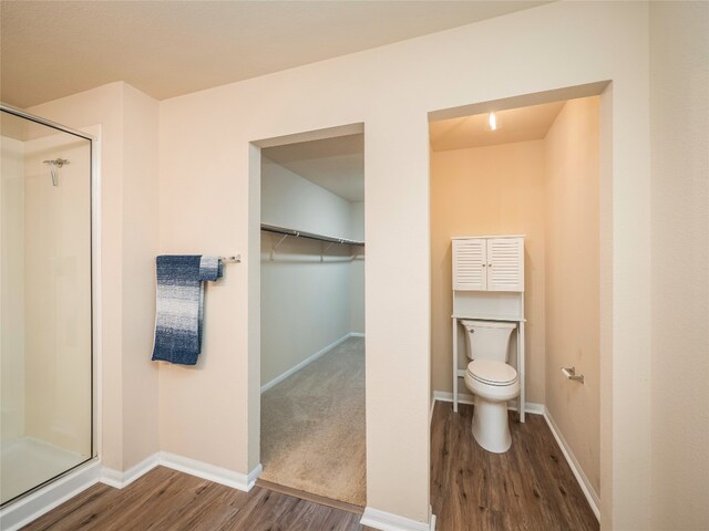 bathroom featuring wood finished floors, toilet, and a shower stall