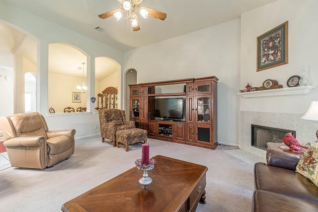 living room featuring visible vents, a ceiling fan, light colored carpet, a tile fireplace, and arched walkways