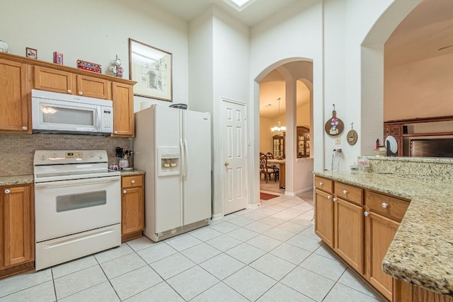 kitchen with white appliances, a high ceiling, brown cabinets, light stone counters, and light tile patterned floors