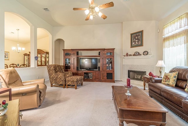 living area featuring light carpet, arched walkways, a tiled fireplace, ceiling fan with notable chandelier, and visible vents