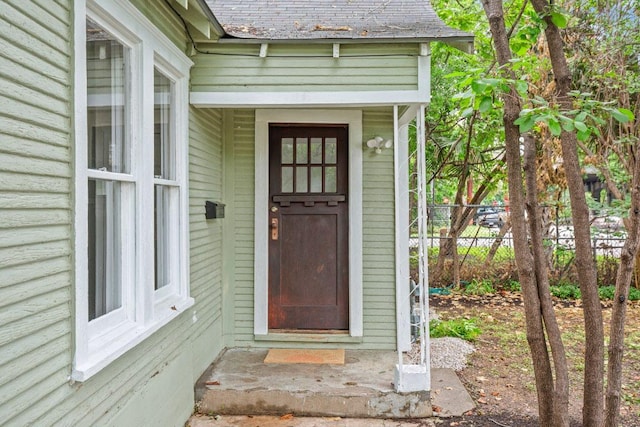 view of exterior entry with fence and roof with shingles