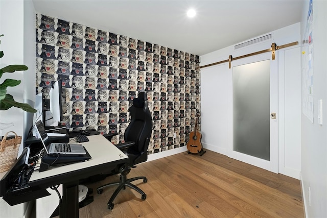 office featuring a barn door, baseboards, wood finished floors, and visible vents