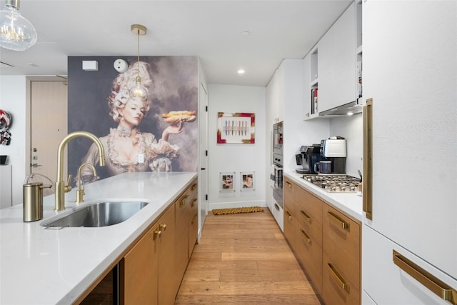 kitchen with light countertops, a sink, light wood-style flooring, hanging light fixtures, and stainless steel appliances
