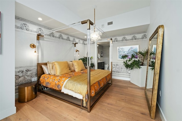 bedroom with baseboards, visible vents, wood finished floors, and ensuite bathroom