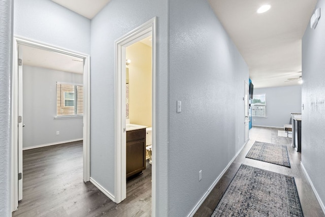 corridor featuring baseboards, a textured wall, and wood finished floors