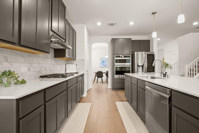 1625 Stinnett Dr, Leander, TX 78641 - kitchen featuring visible vents, a sink, under cabinet range hood, arched walkways, and appliances with stainless steel finishes