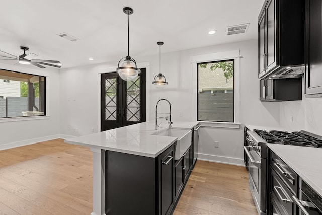 kitchen with high end stainless steel range oven, light wood-type flooring, a sink, a peninsula, and dark cabinetry
