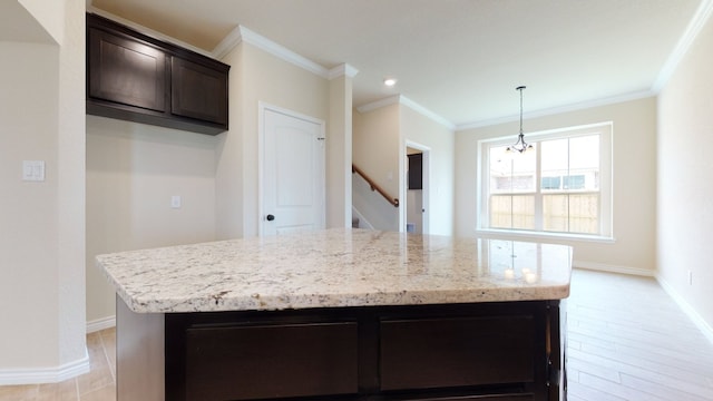 kitchen featuring crown molding, dark brown cabinetry, light stone counters, a center island, and baseboards