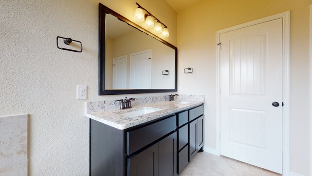 bathroom featuring a sink, tile patterned flooring, a textured wall, and double vanity