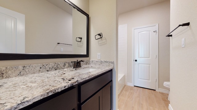 full bathroom with baseboards, wood finished floors, toilet, and vanity