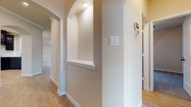 hall featuring light wood-style floors, arched walkways, baseboards, and crown molding