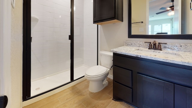 full bathroom featuring a ceiling fan, a shower stall, wood finished floors, vanity, and toilet