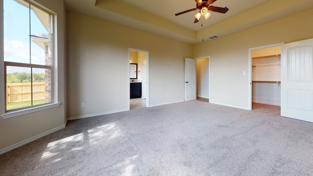 unfurnished bedroom featuring carpet floors, baseboards, a walk in closet, and a tray ceiling