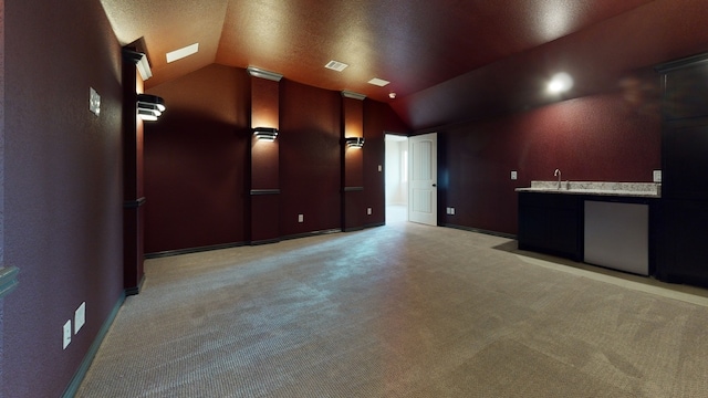 cinema room with indoor wet bar, a textured ceiling, light colored carpet, and lofted ceiling