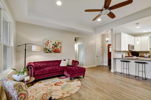 living room featuring ceiling fan, baseboards, a tray ceiling, recessed lighting, and light wood-style flooring