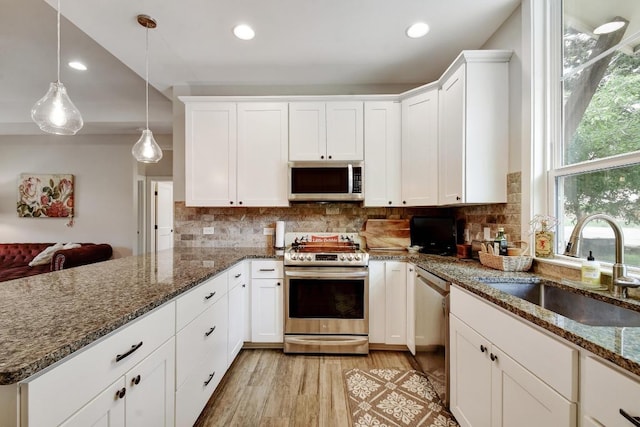 kitchen featuring a sink, a peninsula, light wood-style floors, stainless steel appliances, and white cabinetry