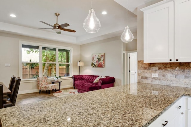 kitchen with a ceiling fan, tasteful backsplash, wood finished floors, light stone counters, and white cabinetry