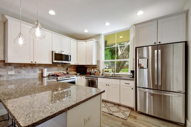 kitchen featuring appliances with stainless steel finishes, tasteful backsplash, a sink, white cabinets, and a peninsula