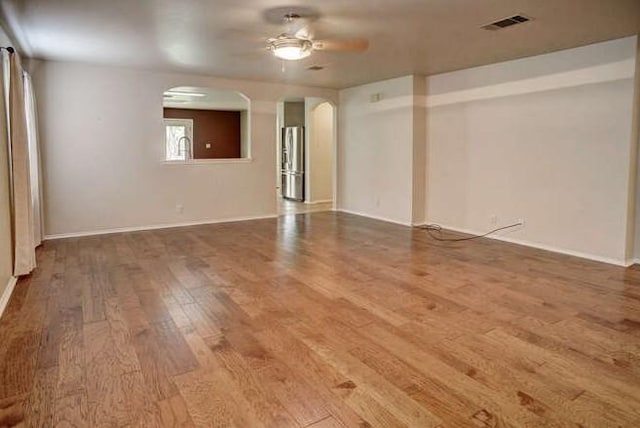 empty room featuring ceiling fan, arched walkways, baseboards, wood finished floors, and visible vents