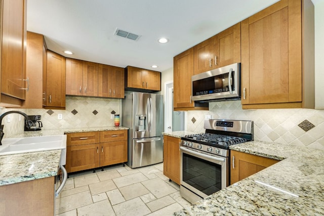 kitchen with brown cabinetry, visible vents, tasteful backsplash, a sink, and stainless steel appliances