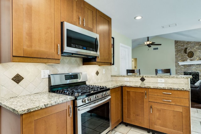 kitchen featuring ceiling fan, brown cabinetry, appliances with stainless steel finishes, light stone counters, and a peninsula