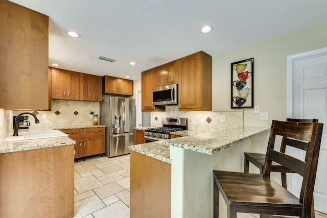 kitchen featuring visible vents, brown cabinets, a sink, a peninsula, and stainless steel appliances