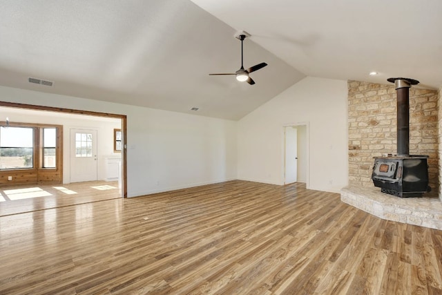 unfurnished living room featuring visible vents, a wood stove, lofted ceiling, ceiling fan, and light wood-style flooring