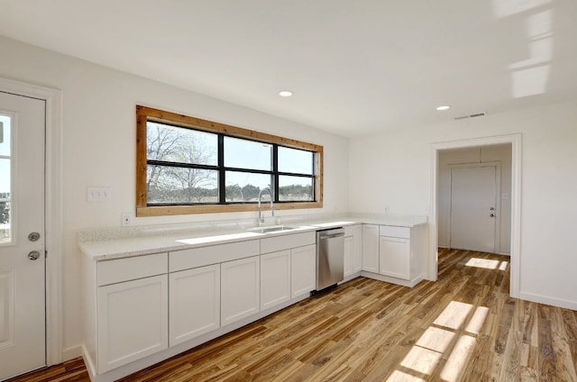 kitchen featuring stainless steel dishwasher, light wood-type flooring, light countertops, white cabinets, and a sink