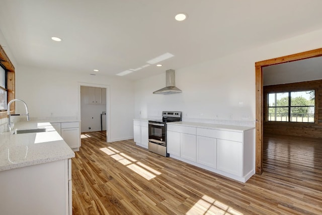kitchen with electric range, a sink, light wood finished floors, wall chimney exhaust hood, and white cabinetry