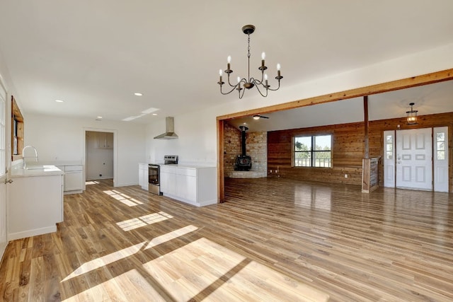 unfurnished living room with a wood stove, a sink, light wood finished floors, a chandelier, and recessed lighting