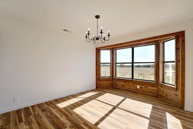 empty room with baseboards, a notable chandelier, wood finished floors, and visible vents