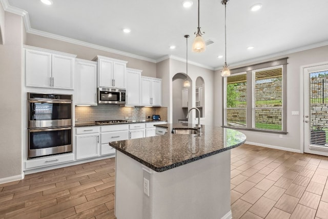 kitchen featuring decorative backsplash, baseboards, arched walkways, a sink, and appliances with stainless steel finishes